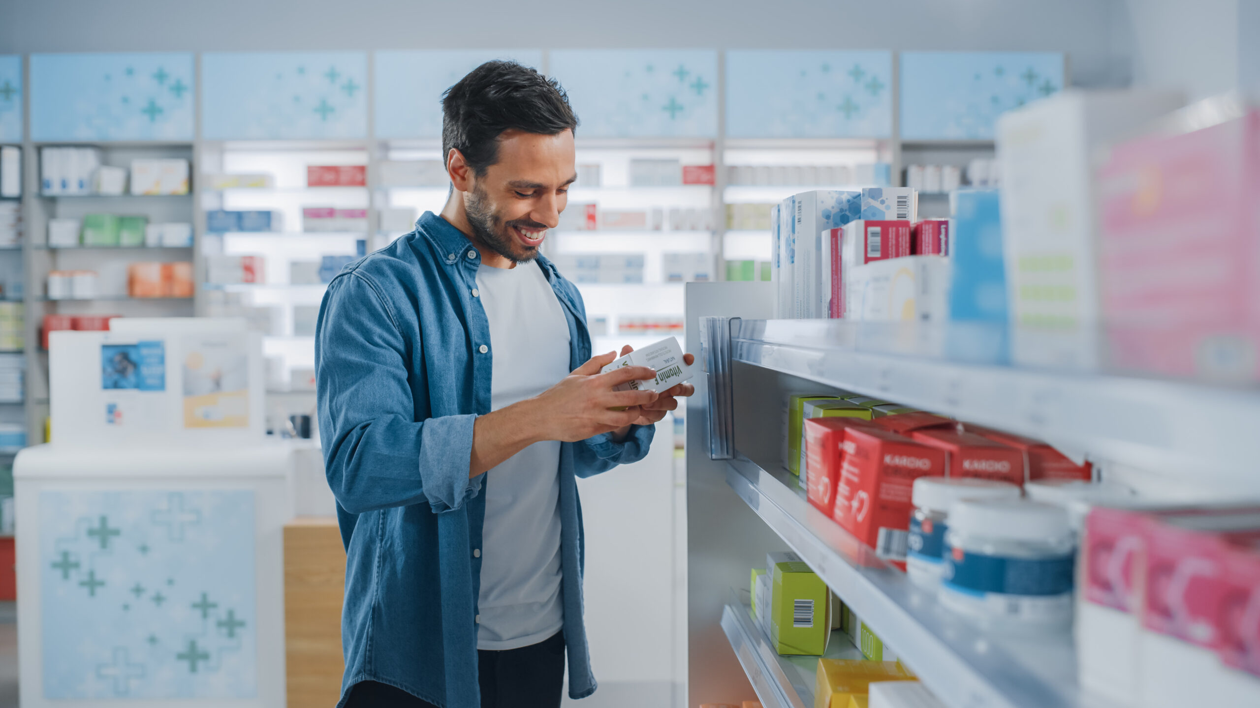 Ein Mann mittleren Alters steht vor einem Regal in einer Apotheke und hat ein Produkt in den Händen, dass er aufmerksam studiert.